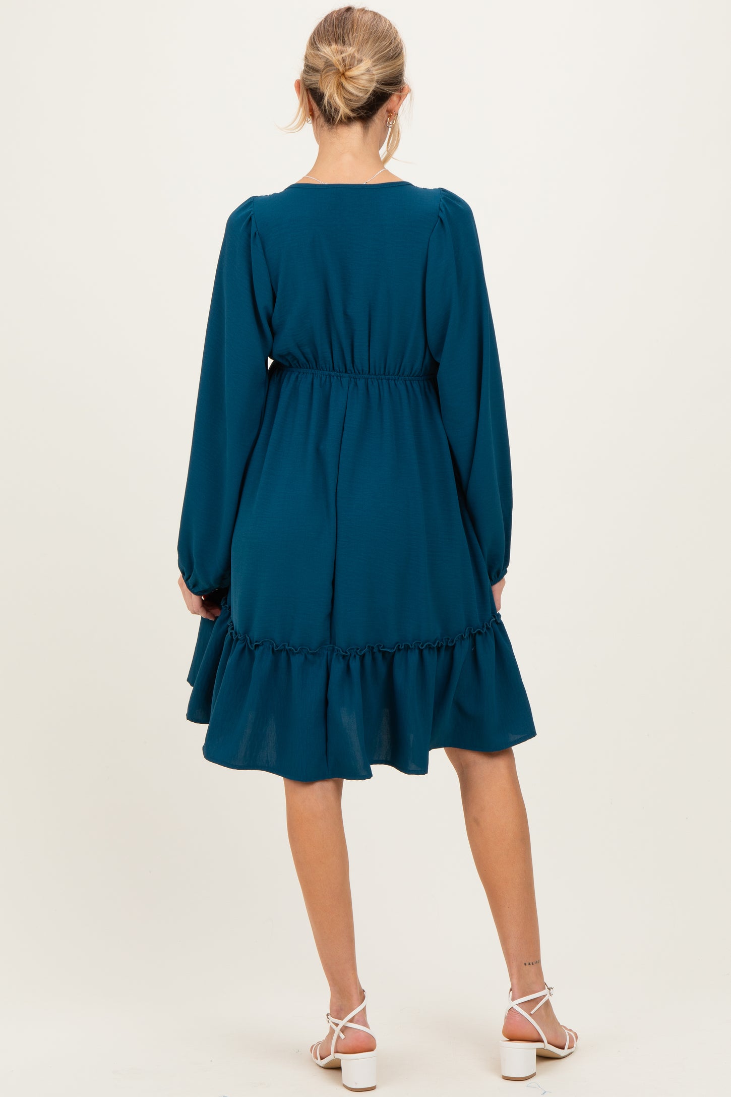 woman wearing a teal long sleeve maternity dress with a ruffled hem and cinched waist, seen from the back