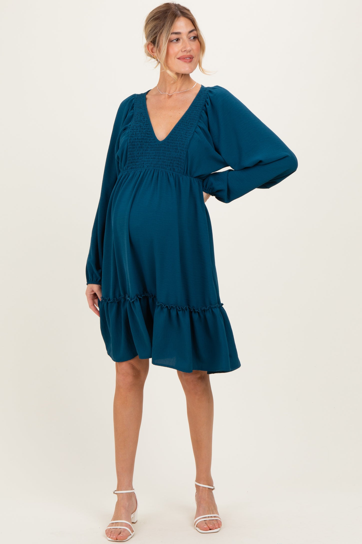 woman wearing a teal maternity dress with a deep v-neck, long sleeves, and a ruffled hem, showing her baby bump