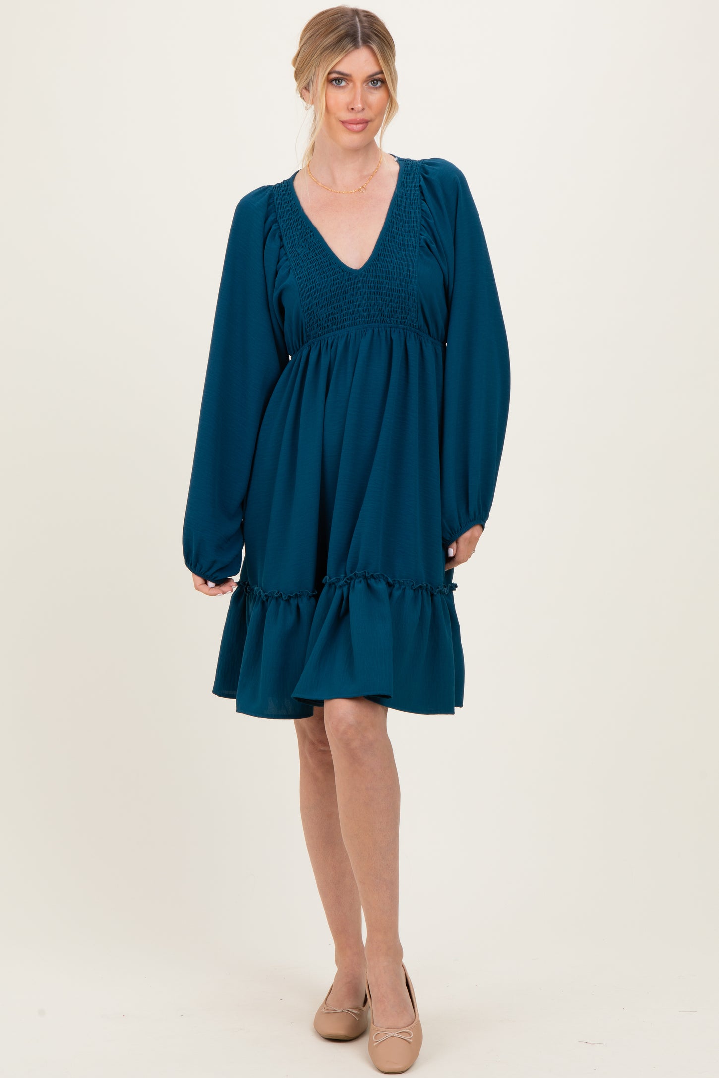 woman wearing a teal smocked waist long sleeve dress with a flared skirt and v-neckline