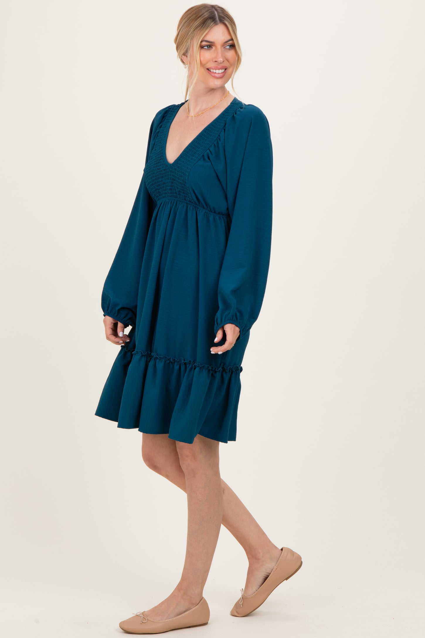 woman wearing a teal smocked v-neck dress with long puff sleeves and ruffled hem, standing in a side pose