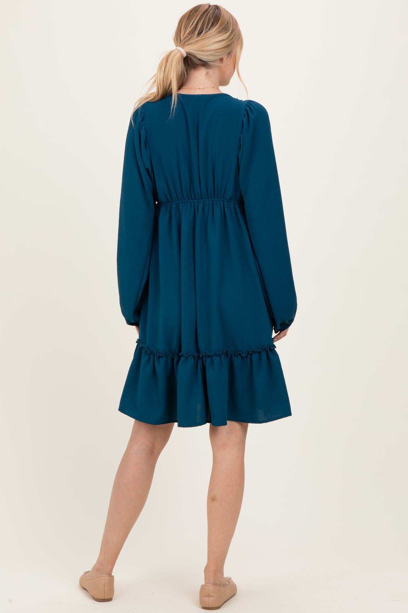 woman wearing a teal long sleeve dress with a tiered ruffle hem and cinched waist, viewed from the back