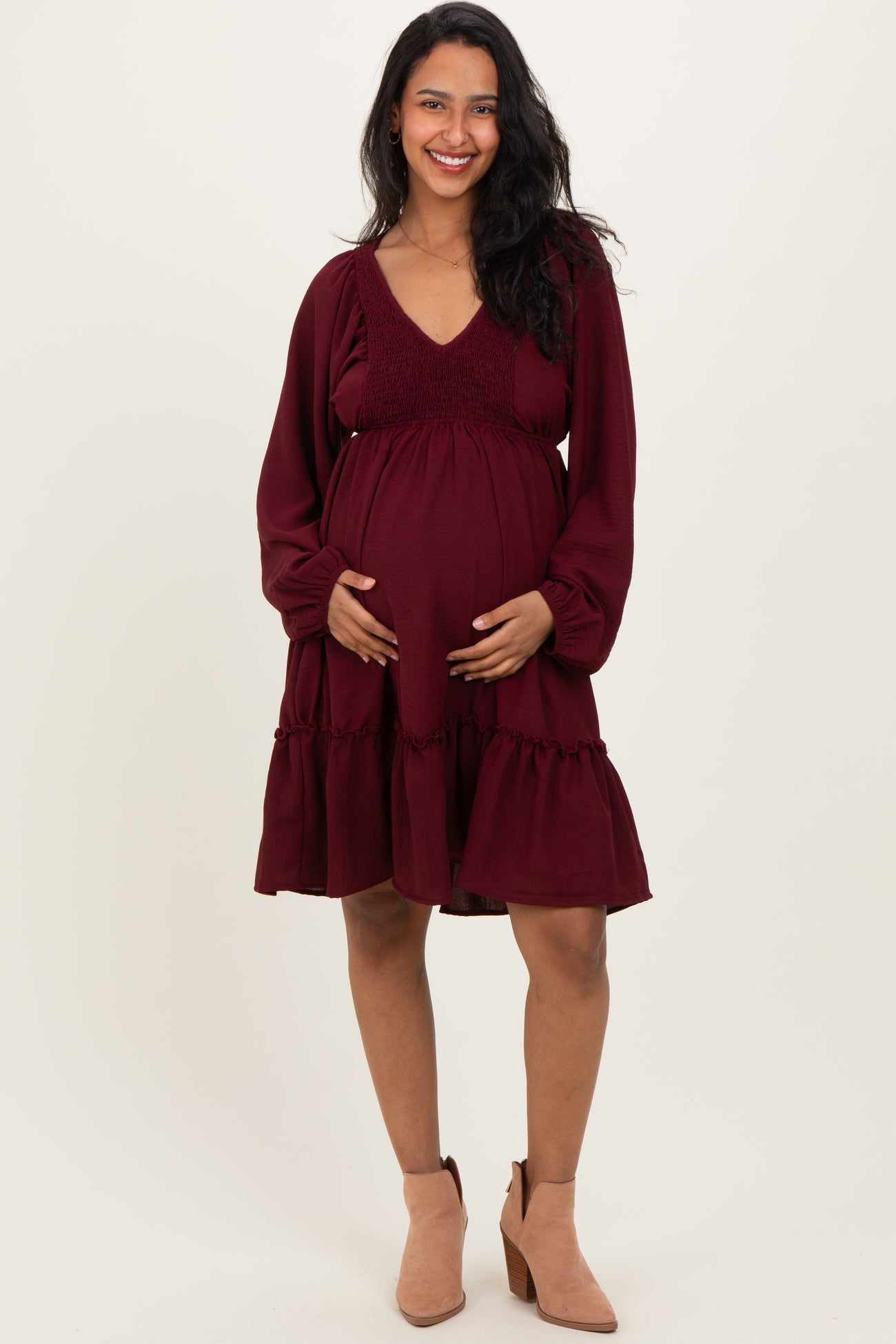 woman wearing a burgundy maternity dress with a smocked bodice and flared skirt, holding her baby bump