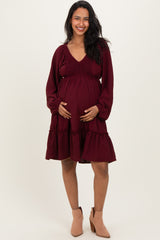 woman wearing a burgundy maternity dress with a smocked bodice and flared skirt, holding her baby bump