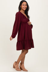 woman wearing a burgundy maternity dress with a ruffled hem and a v-neck, showing her baby bump