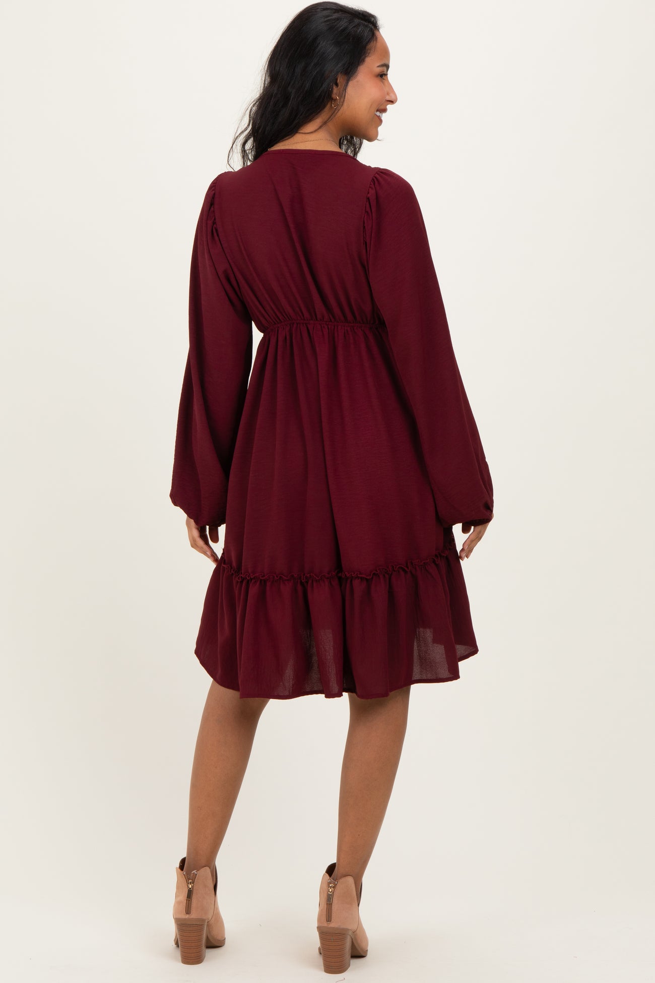 woman wearing a burgundy maternity dress with long sleeves and a ruffled hem, showing her baby bump from the back
