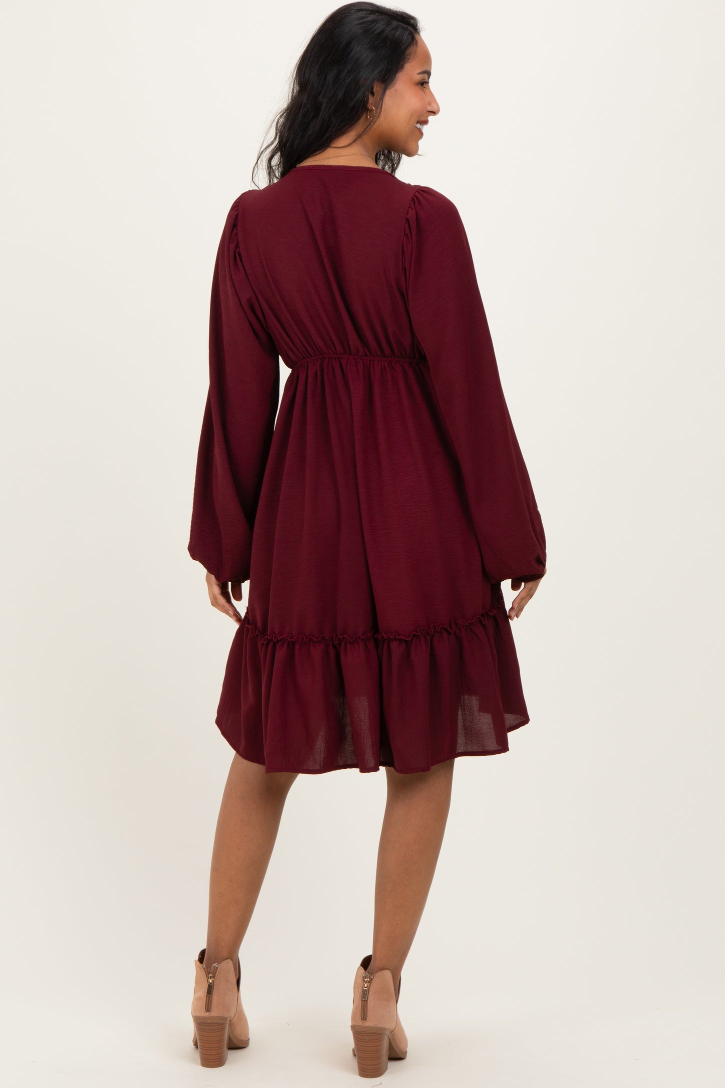 woman wearing a burgundy maternity dress with long sleeves and a ruffled hem, showing her baby bump from the back