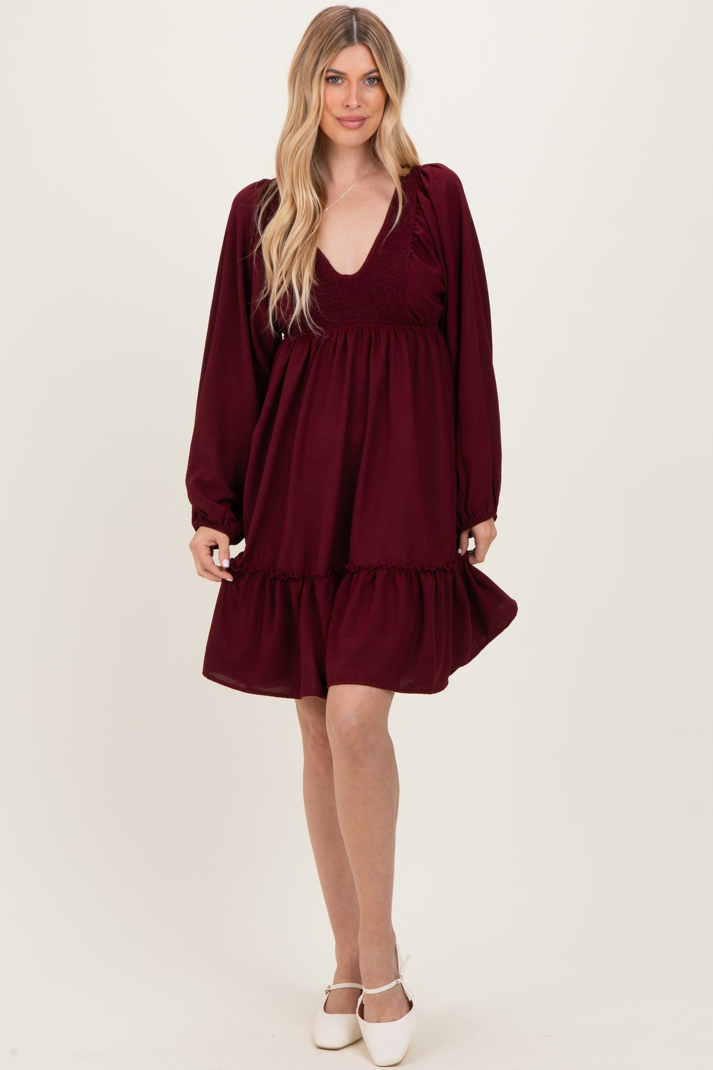 woman wearing a burgundy long sleeve smocked dress with a tiered skirt and deep v-neckline