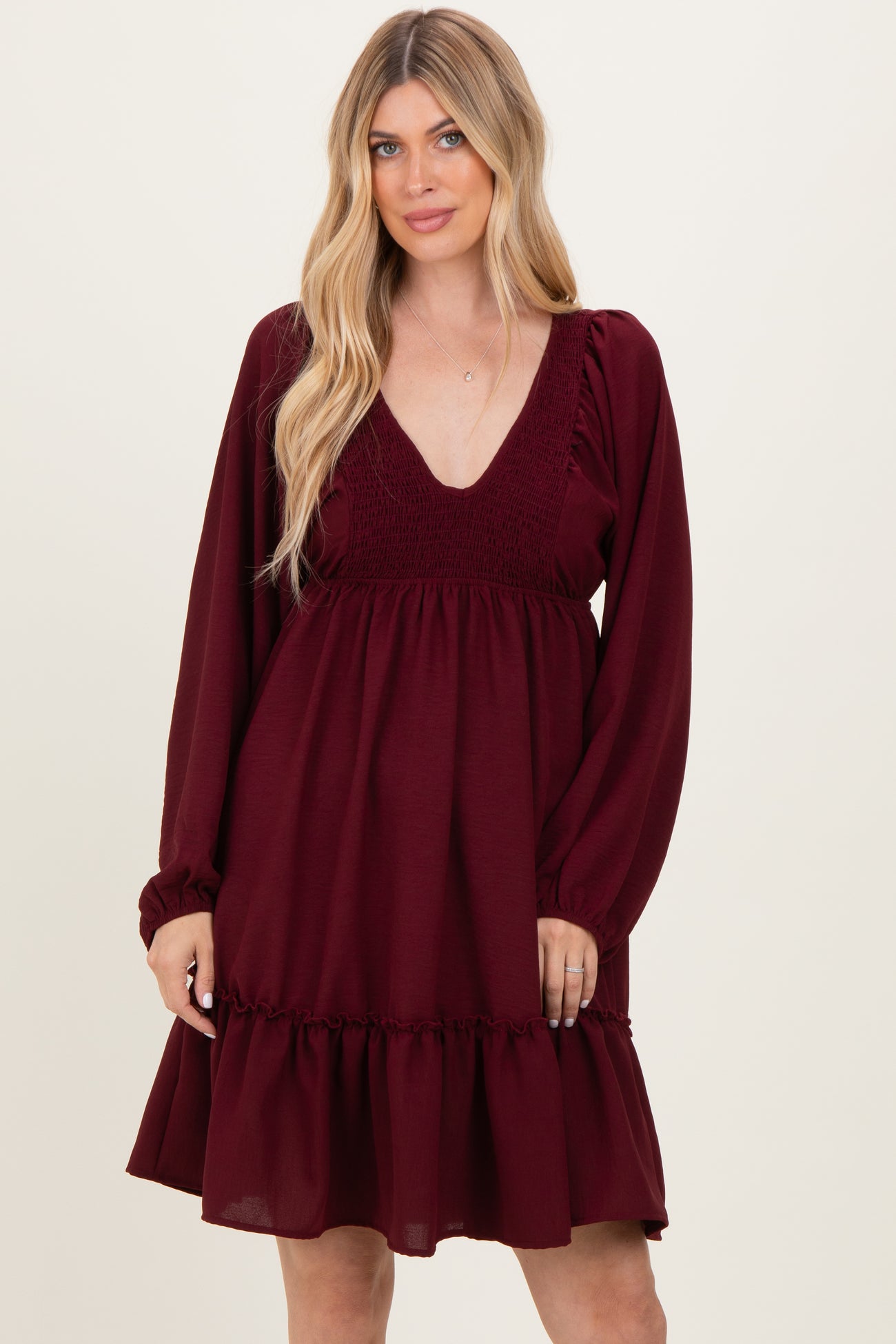woman wearing a burgundy long sleeve dress with a deep v-neck and smocked bodice, featuring a ruffled hemline