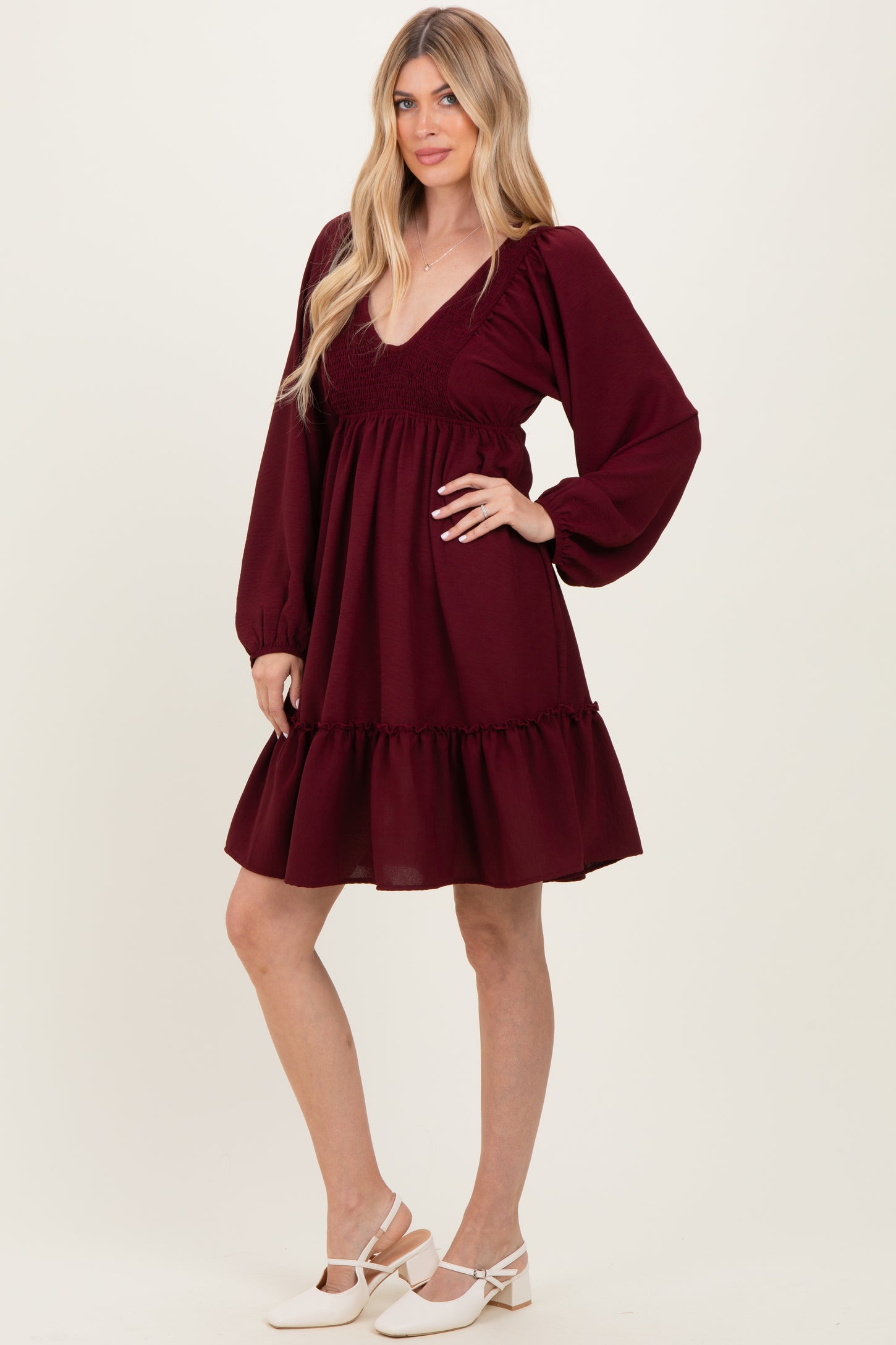 woman wearing a burgundy short sleeve dress with a deep v-neck and puff sleeves, styled with a ruffled hem