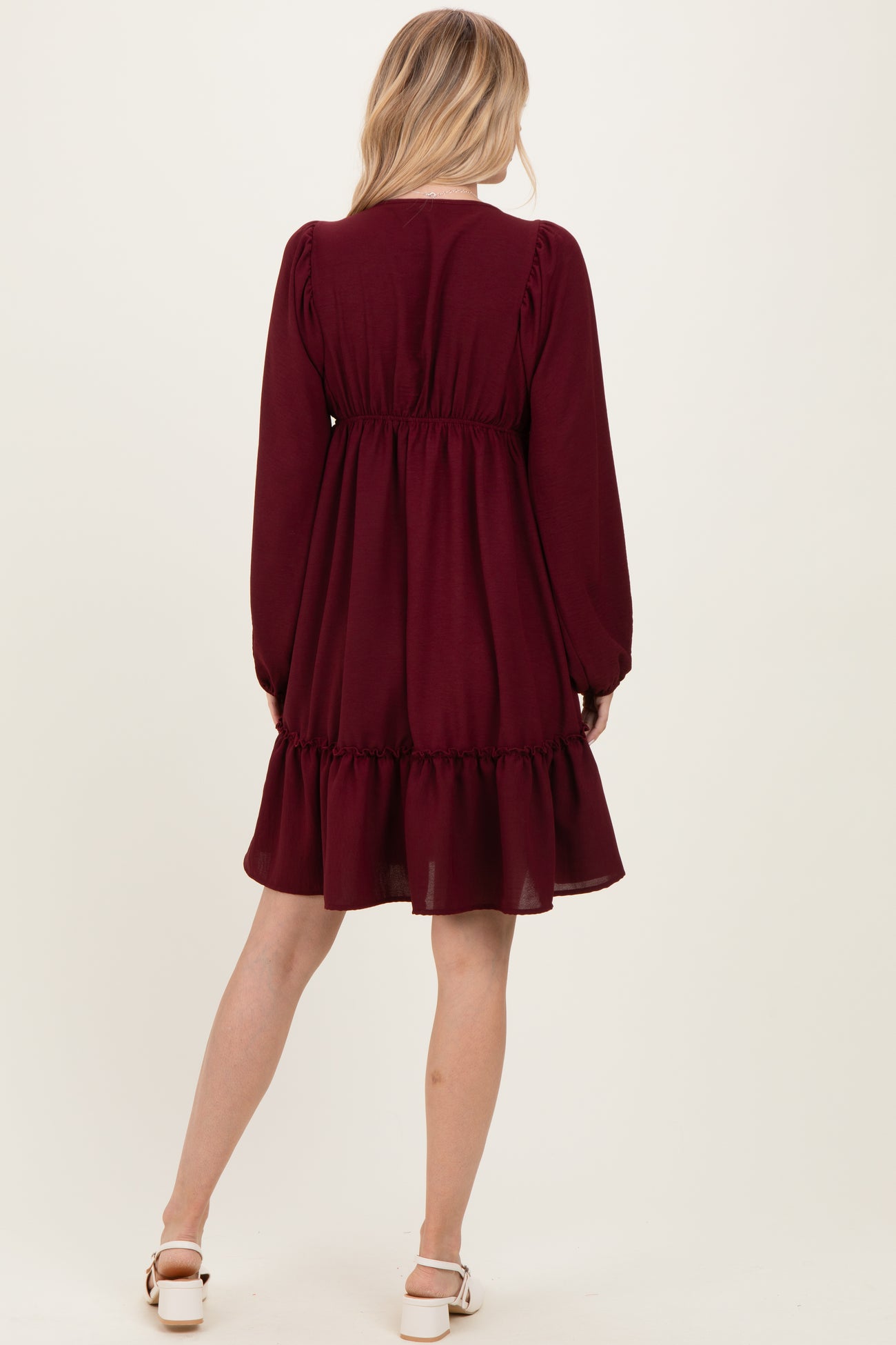 woman wearing a burgundy long sleeve dress with a ruffled hem and an elastic waist, viewed from the back