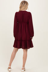 woman wearing a burgundy long sleeve dress with a ruffled hem and an elastic waist, viewed from the back