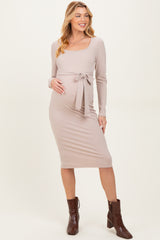 woman wearing a blush pink ribbed maternity dress with a square neckline and a tie waist, showing her baby bump