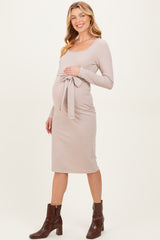 woman wearing a light beige long sleeve maternity dress with a tie waist and a visible baby bump