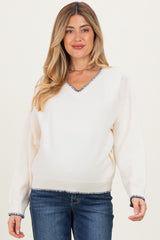 woman wearing a cream v-neck maternity sweater with navy striped detailing at the neckline and hem, paired with jeans