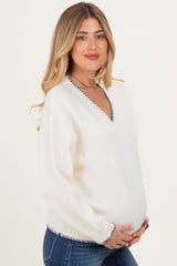 woman wearing a cream maternity sweater with a v-neck and navy stitching, showing her baby bump