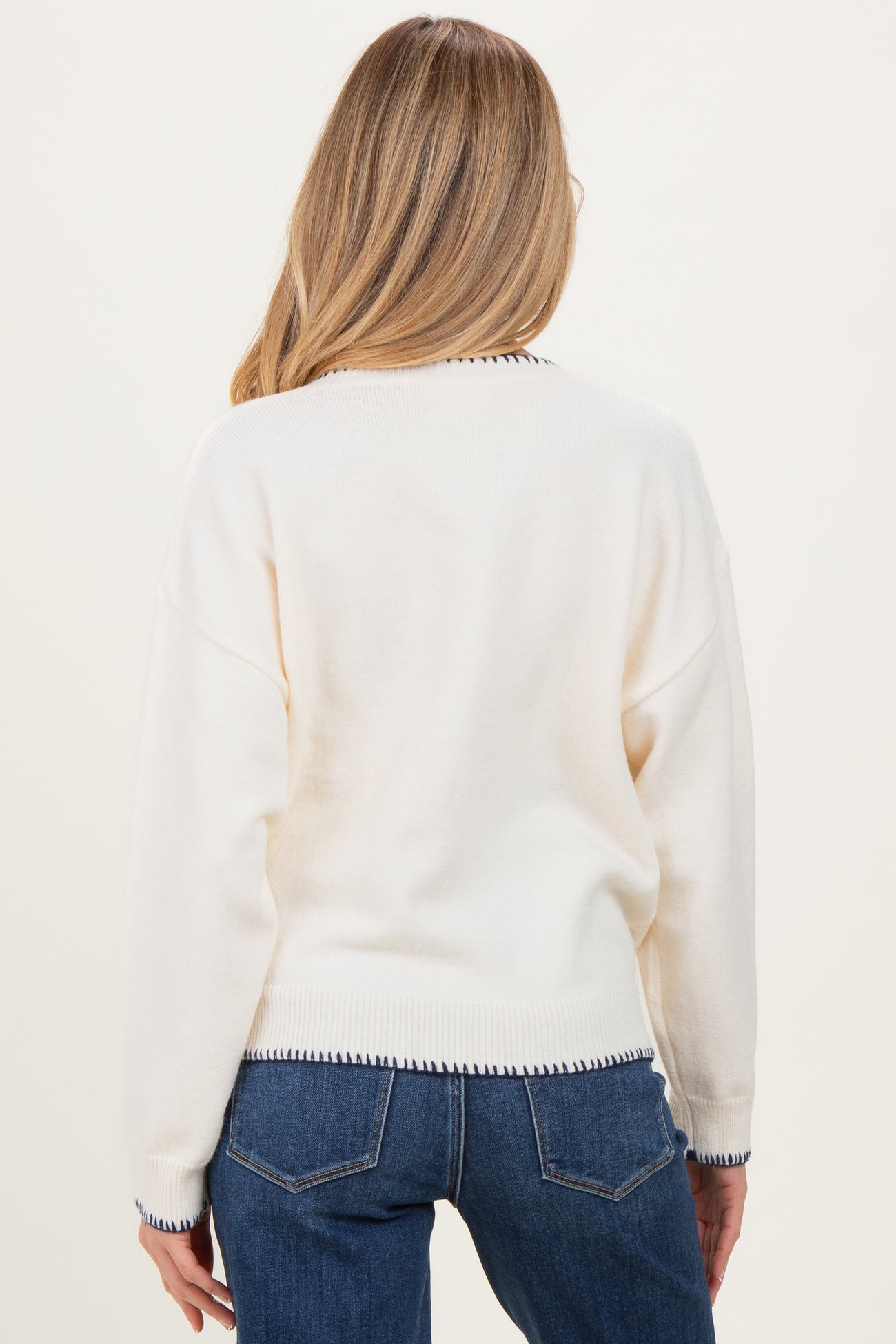 woman wearing a cream maternity sweater with navy trim, viewed from the back, featuring a relaxed fit and long sleeves