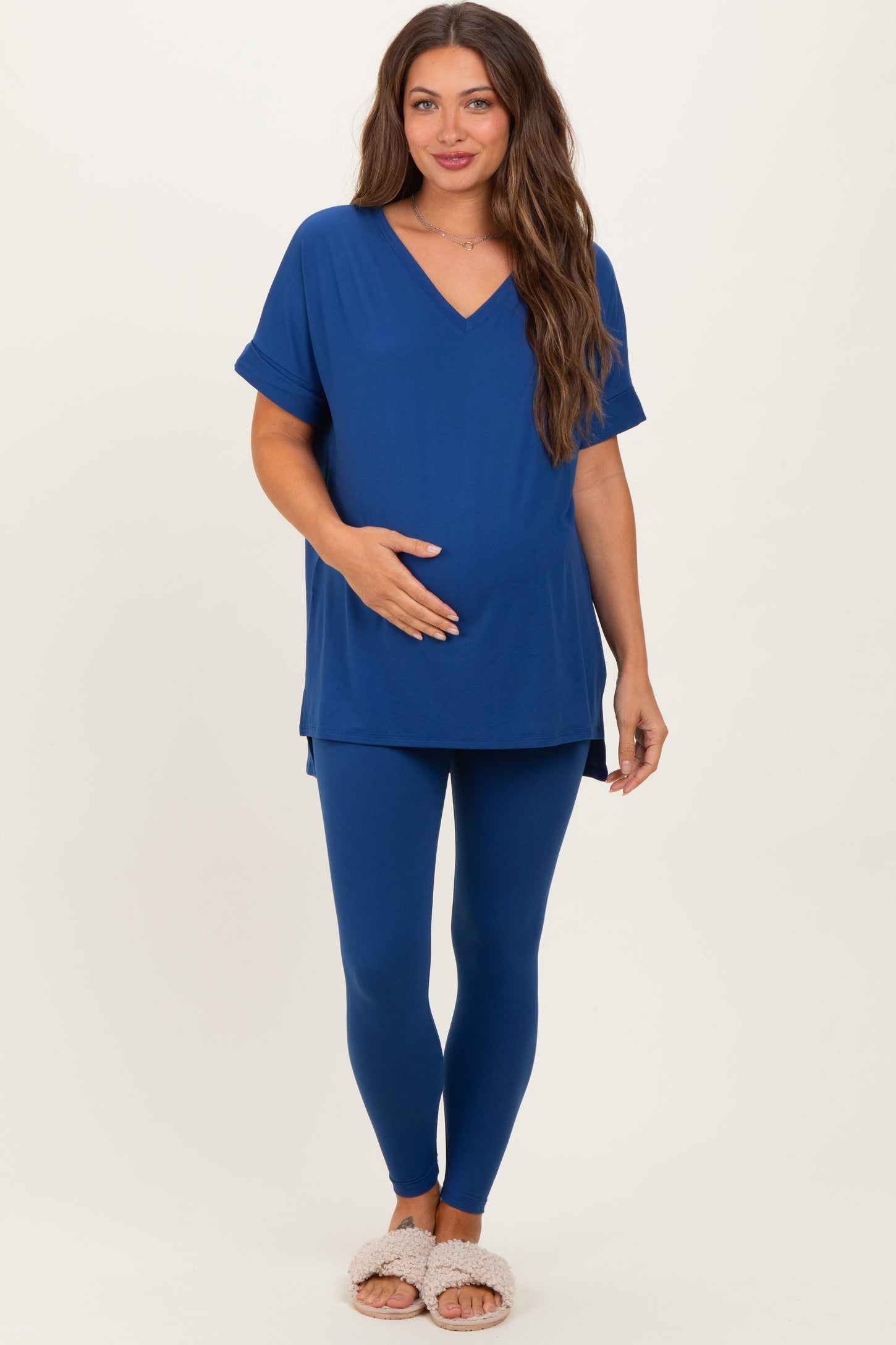 woman wearing a blue maternity top and matching leggings, holding her baby bump