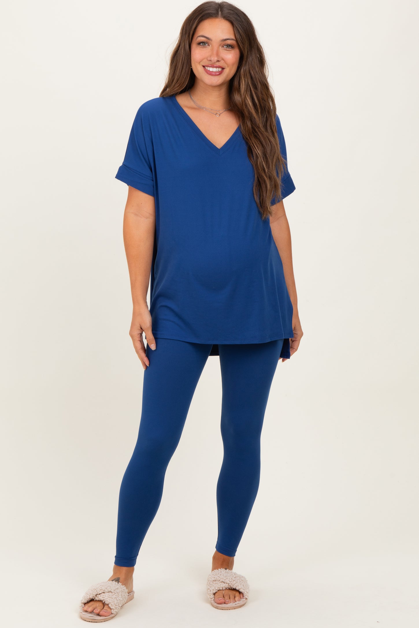 woman wearing a blue maternity top and matching leggings, showing her baby bump, paired with cozy slipper shoes
