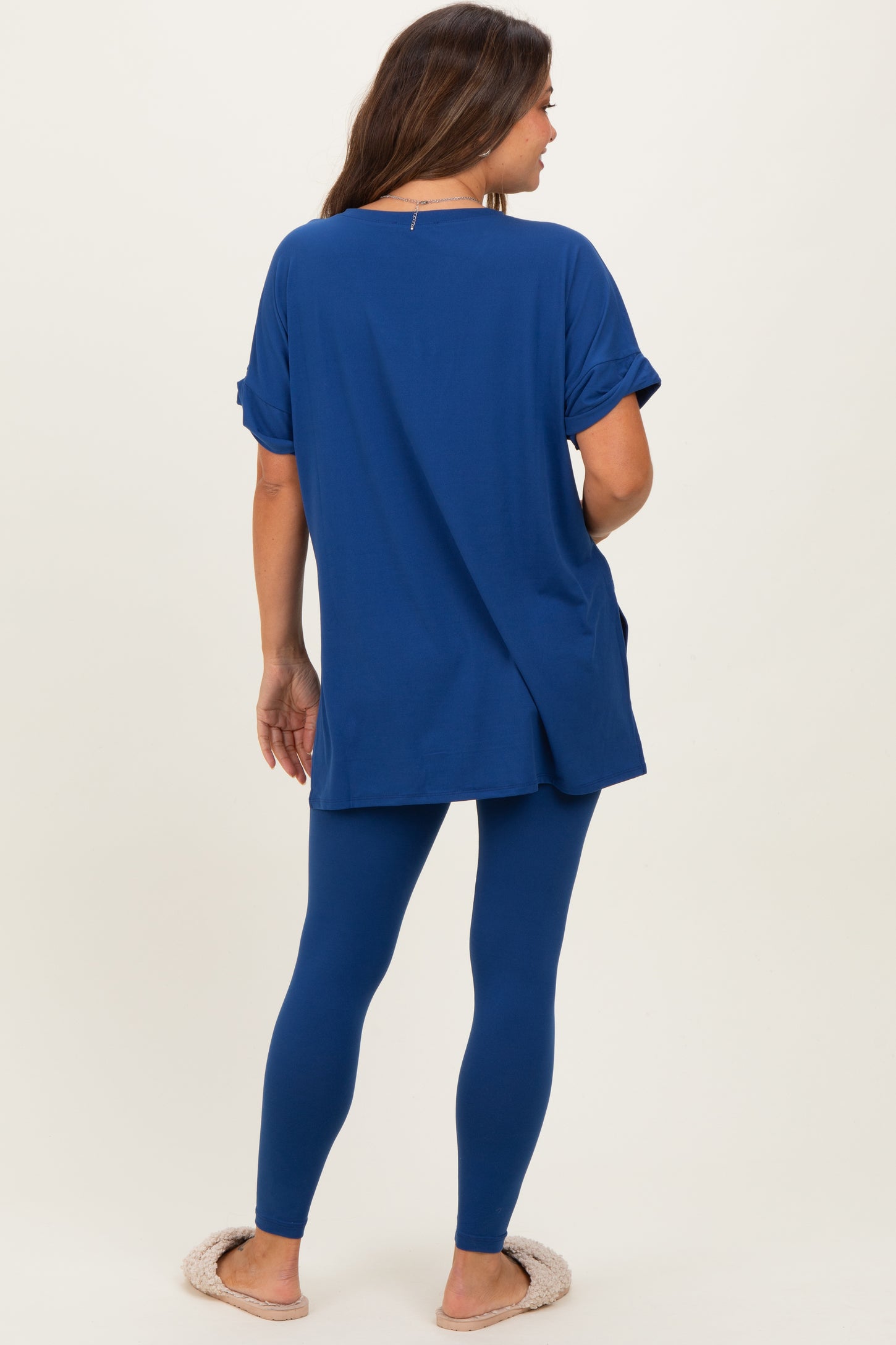 woman wearing a blue maternity top with rolled sleeves and matching leggings, showing a baby bump from the back