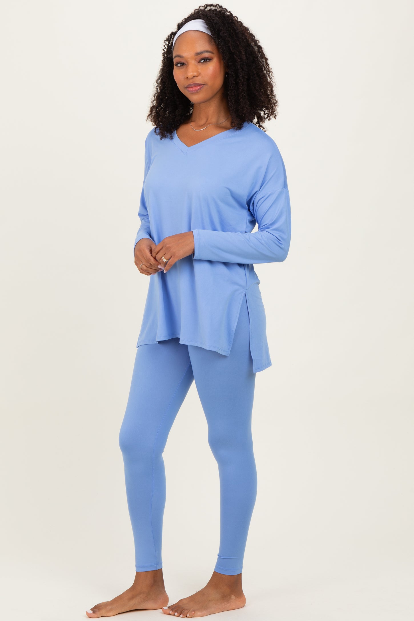 woman wearing a light blue long sleeve v-neck top and matching leggings, standing barefoot with a headband