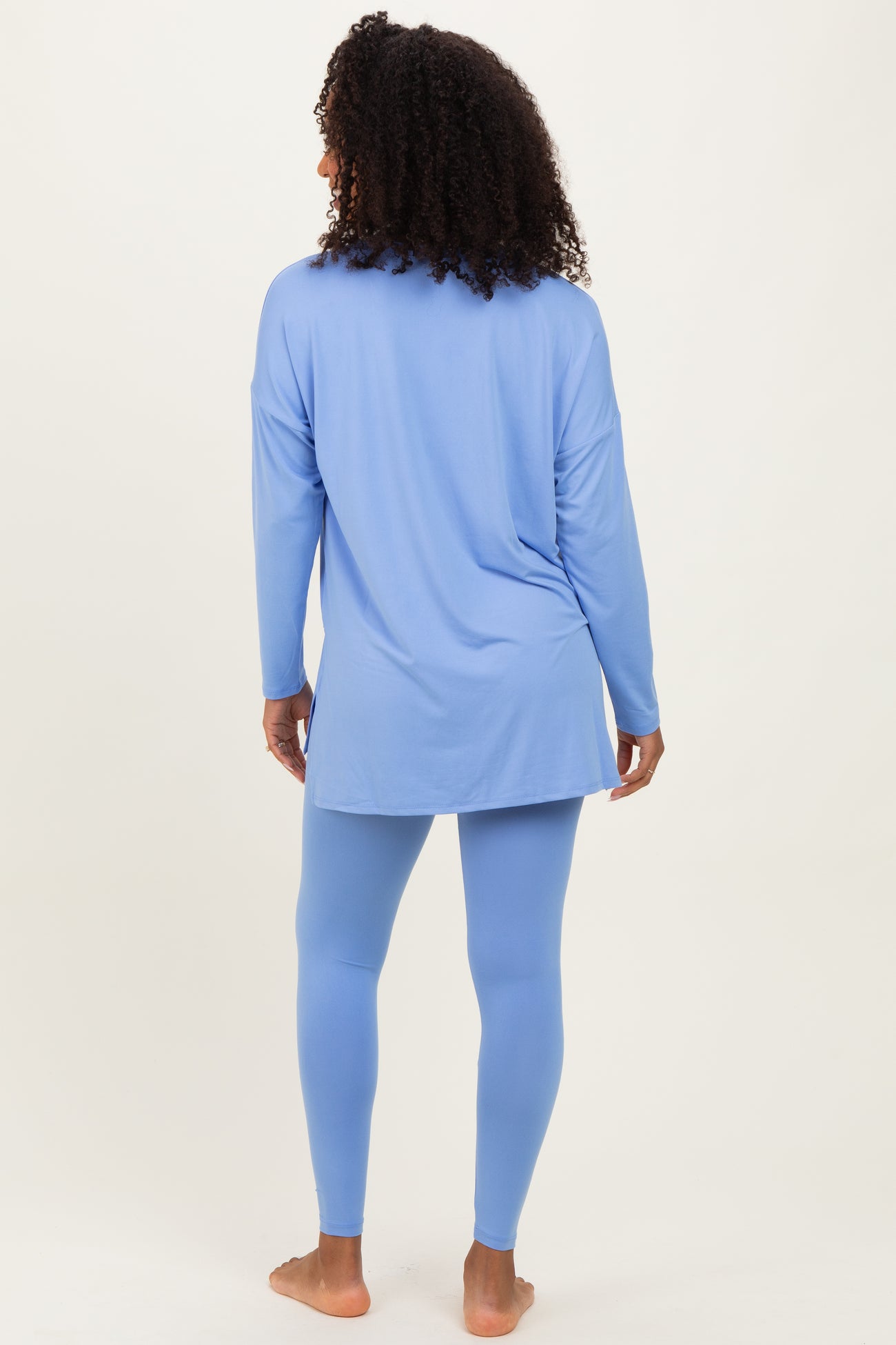woman wearing a light blue long sleeve tunic top and matching leggings, standing with her back to the camera