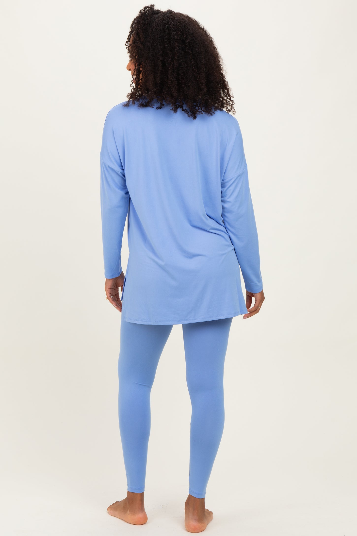 woman wearing a light blue long sleeve tunic top and matching leggings, standing with her back to the camera