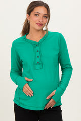 woman wearing a green long sleeve maternity top with buttons and holding her baby bump