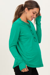 woman wearing a green long sleeve maternity top with a henley neckline and visible baby bump
