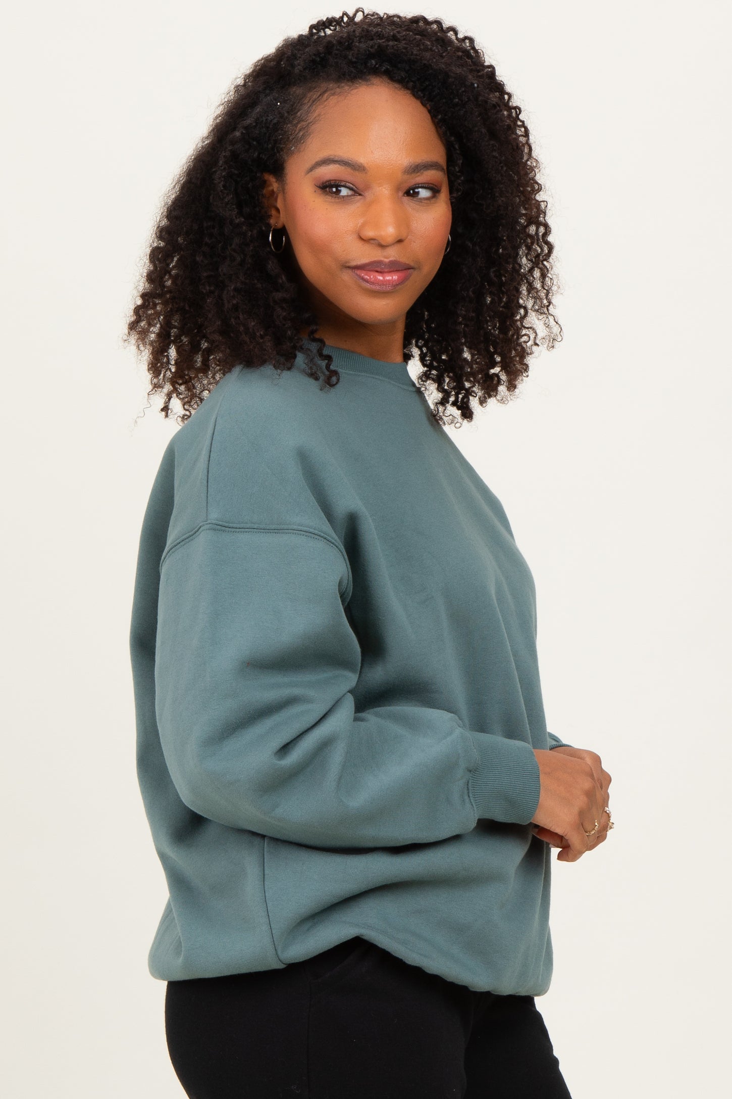 woman wearing an oversized teal sweatshirt with a relaxed fit and crew neckline, styled with black pants