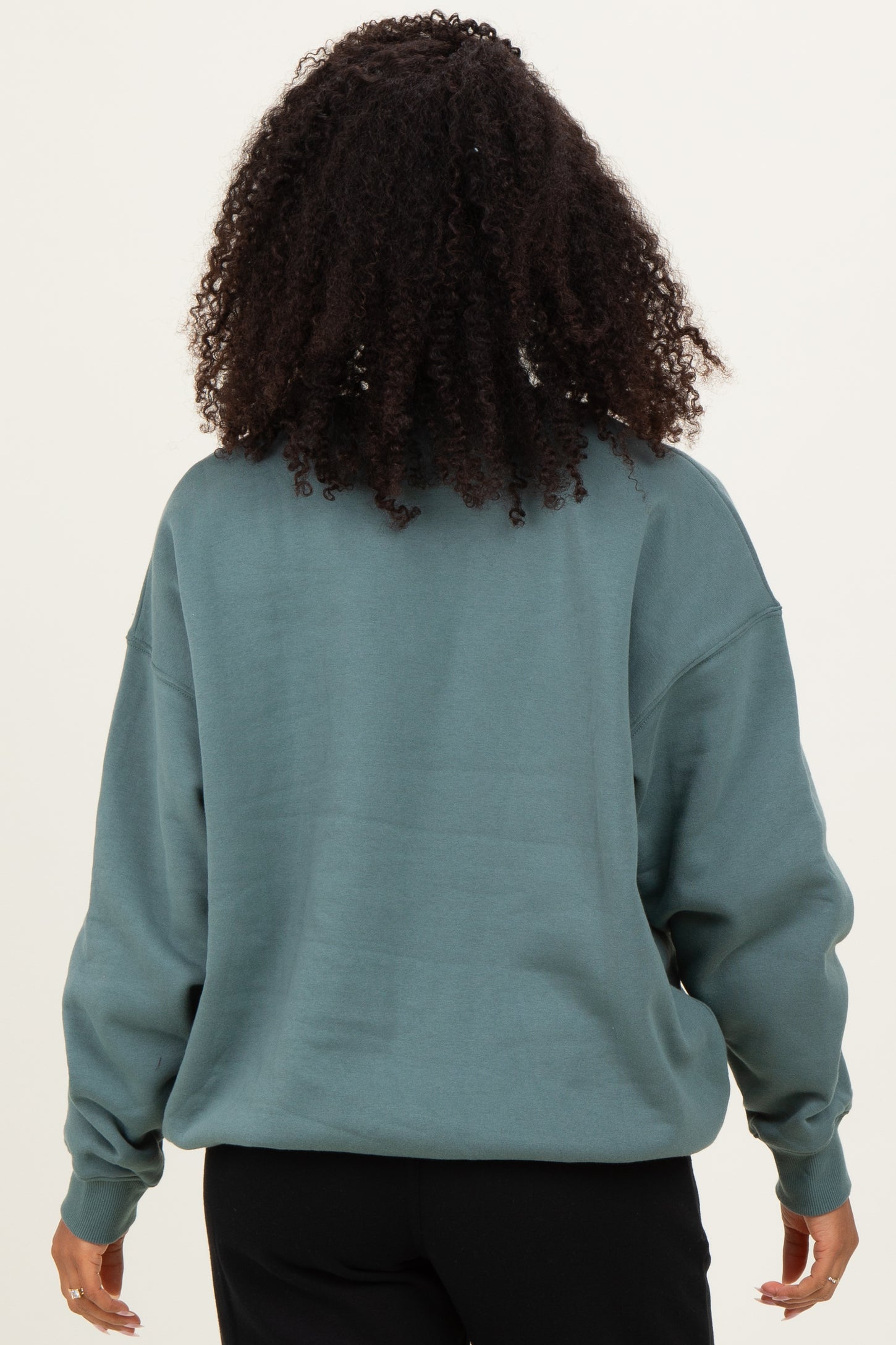 woman wearing a green oversized sweatshirt, viewed from the back, with loose-fitting sleeves and a relaxed silhouette