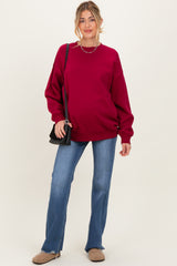 woman wearing a burgundy maternity sweatshirt and blue flared jeans, holding a black bag and showing her baby bump