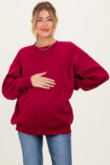 woman wearing a burgundy oversized maternity sweatshirt and holding her baby bump