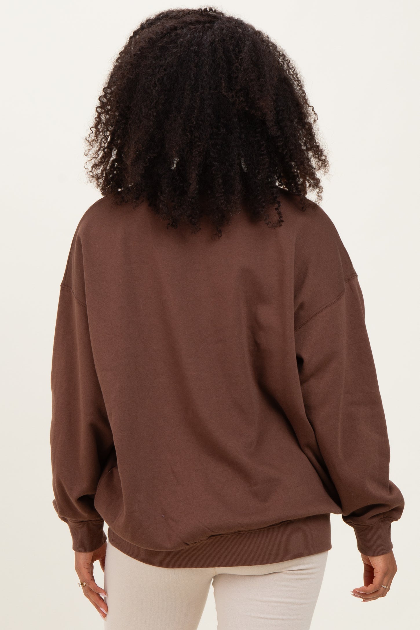woman wearing a brown oversized sweatshirt with long sleeves and a relaxed fit, viewed from the back