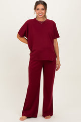 woman wearing a burgundy maternity loungewear set with a short sleeve top and wide-leg pants, showing her baby bump