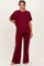 woman wearing a burgundy maternity loungewear set with a short sleeve top and wide-leg pants, showing her baby bump