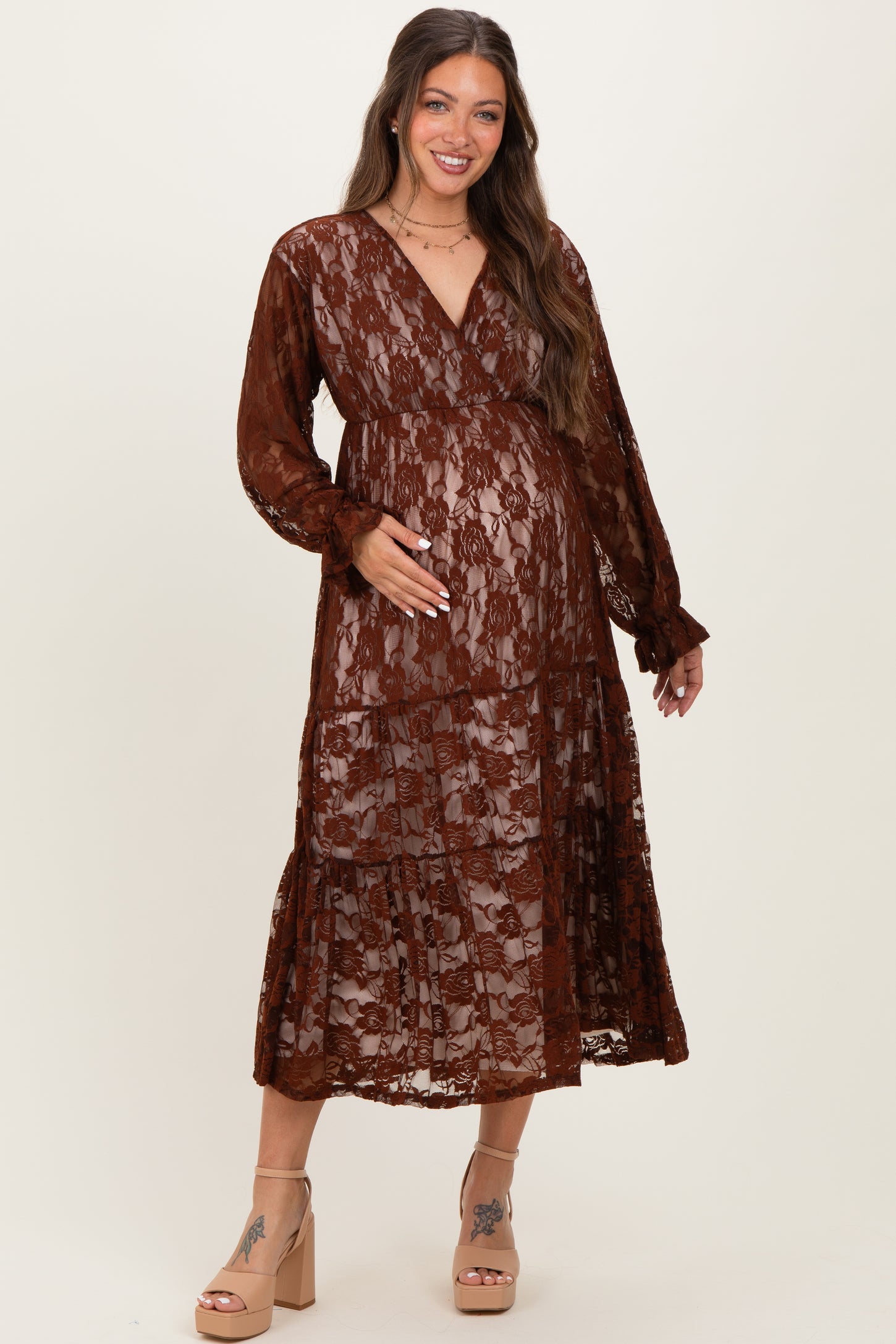 woman wearing a rust lace maternity dress with a tiered skirt and deep v-neck, holding her baby bump