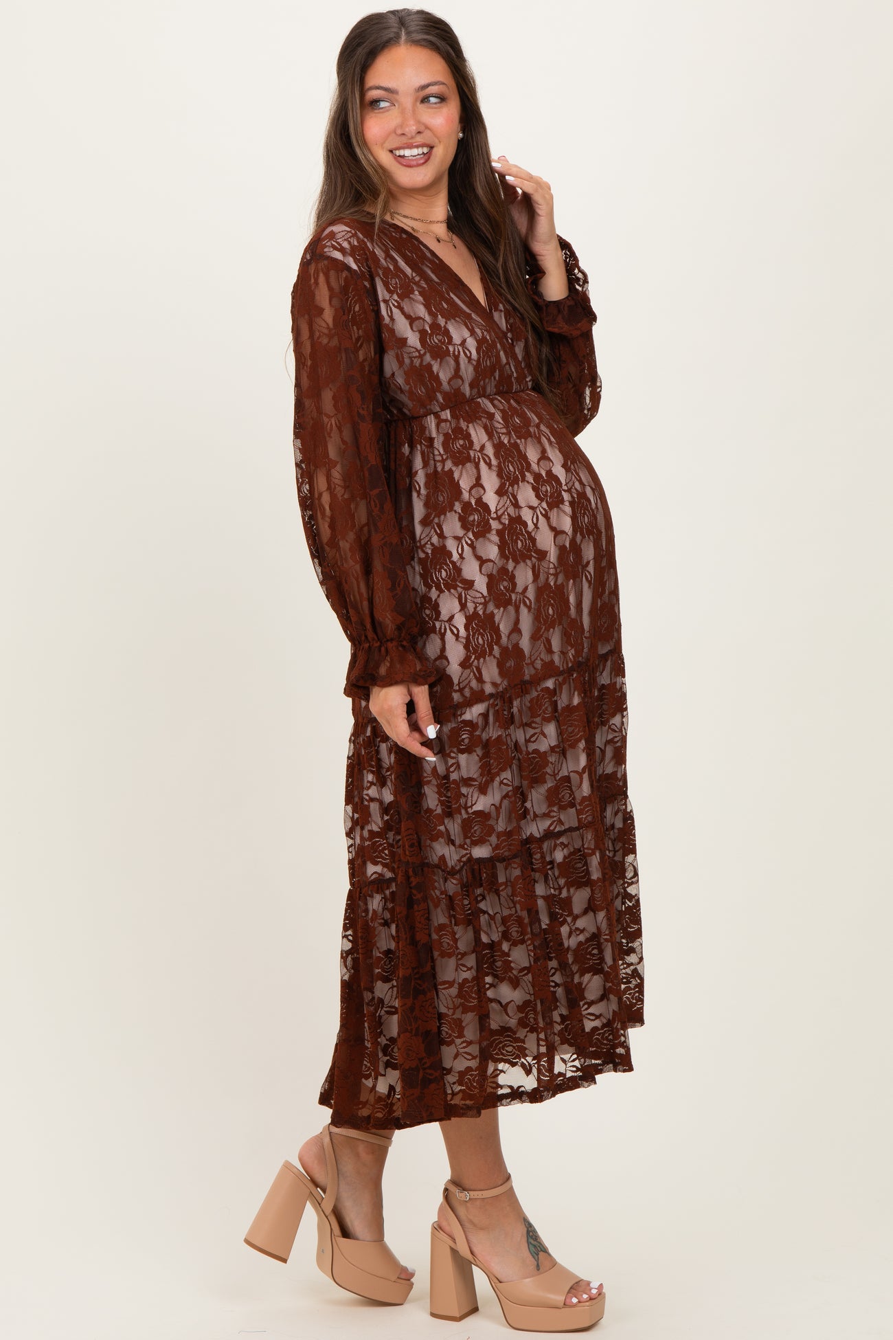 woman wearing a brown lace maternity dress with a tiered skirt and long sleeves, showcasing a visible baby bump