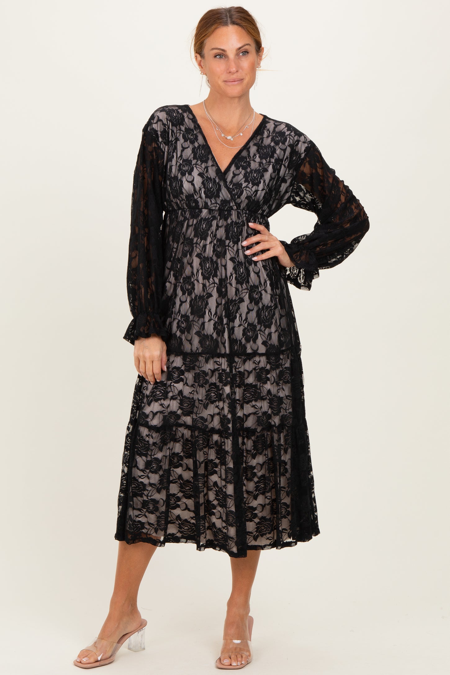 woman wearing a black lace midi dress with long sleeves and a v-neckline, styled with clear heeled sandals
