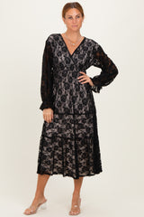woman wearing a black lace midi dress with long sleeves and a v-neckline, styled with clear heeled sandals