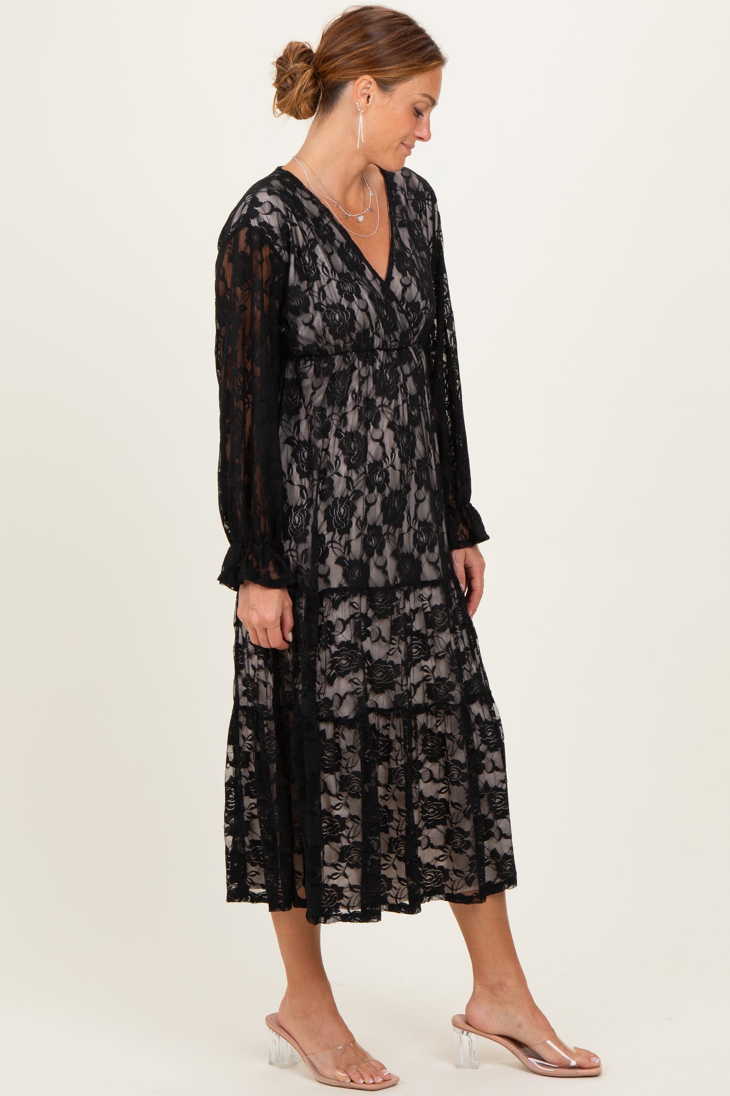 woman wearing a black lace midi dress with long sleeves and a layered skirt, styled with clear heeled sandals