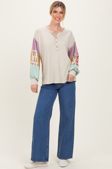 woman wearing a cream ribbed long sleeve henley top with patterned color block sleeves and wide leg blue jeans