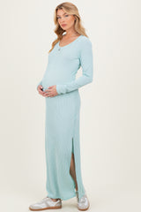 woman wearing a light teal long sleeve maternity dress with a side slit and cradling her baby bump
