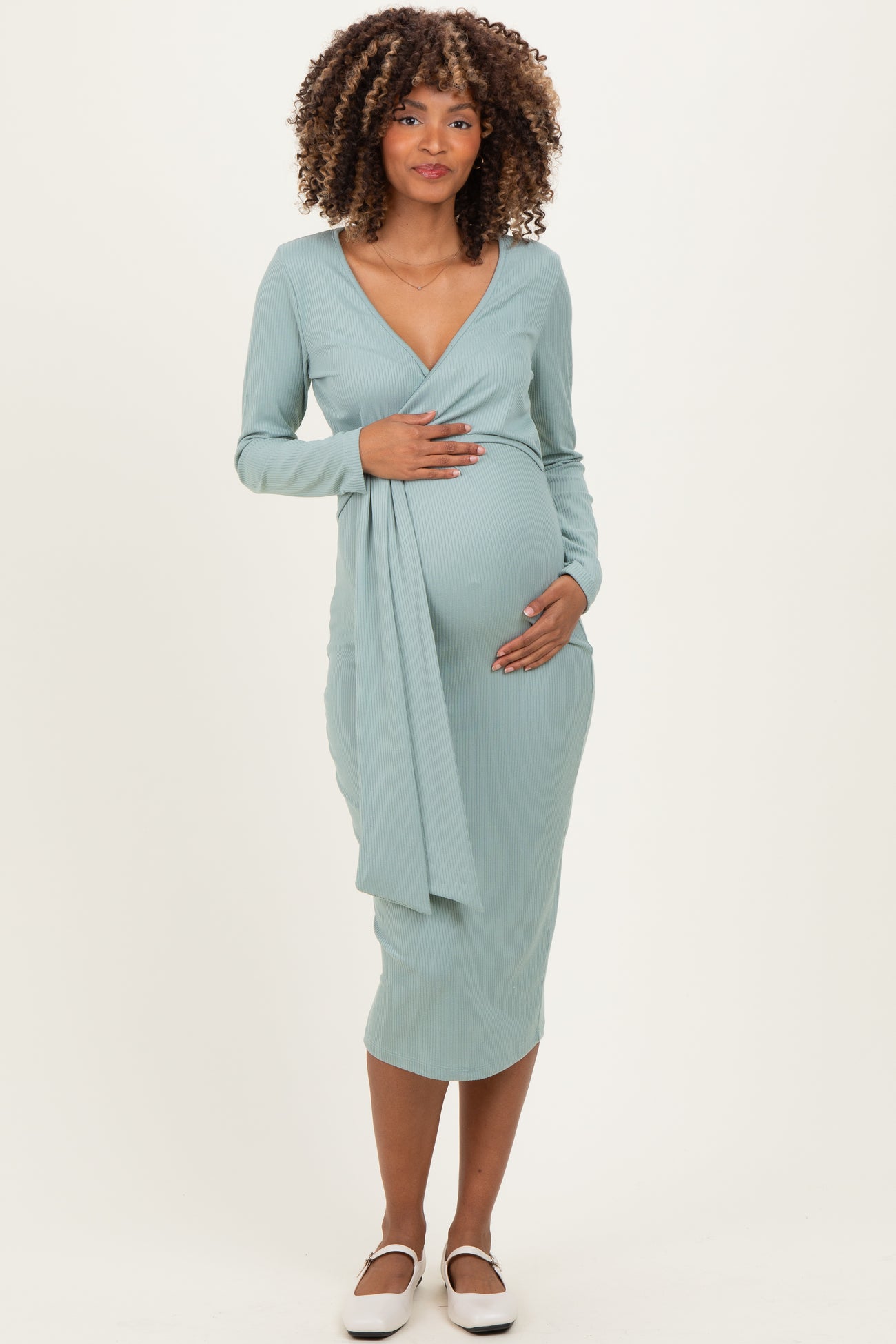 woman wearing a light blue maternity wrap dress with long sleeves, gently holding her baby bump