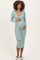 woman wearing a light blue maternity wrap dress with long sleeves, gently holding her baby bump