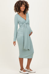 woman wearing a sage green long sleeve maternity dress with a tie at the waist and holding her baby bump