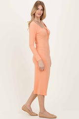 woman wearing a ribbed midi dress in peach with long sleeves and a scoop neckline