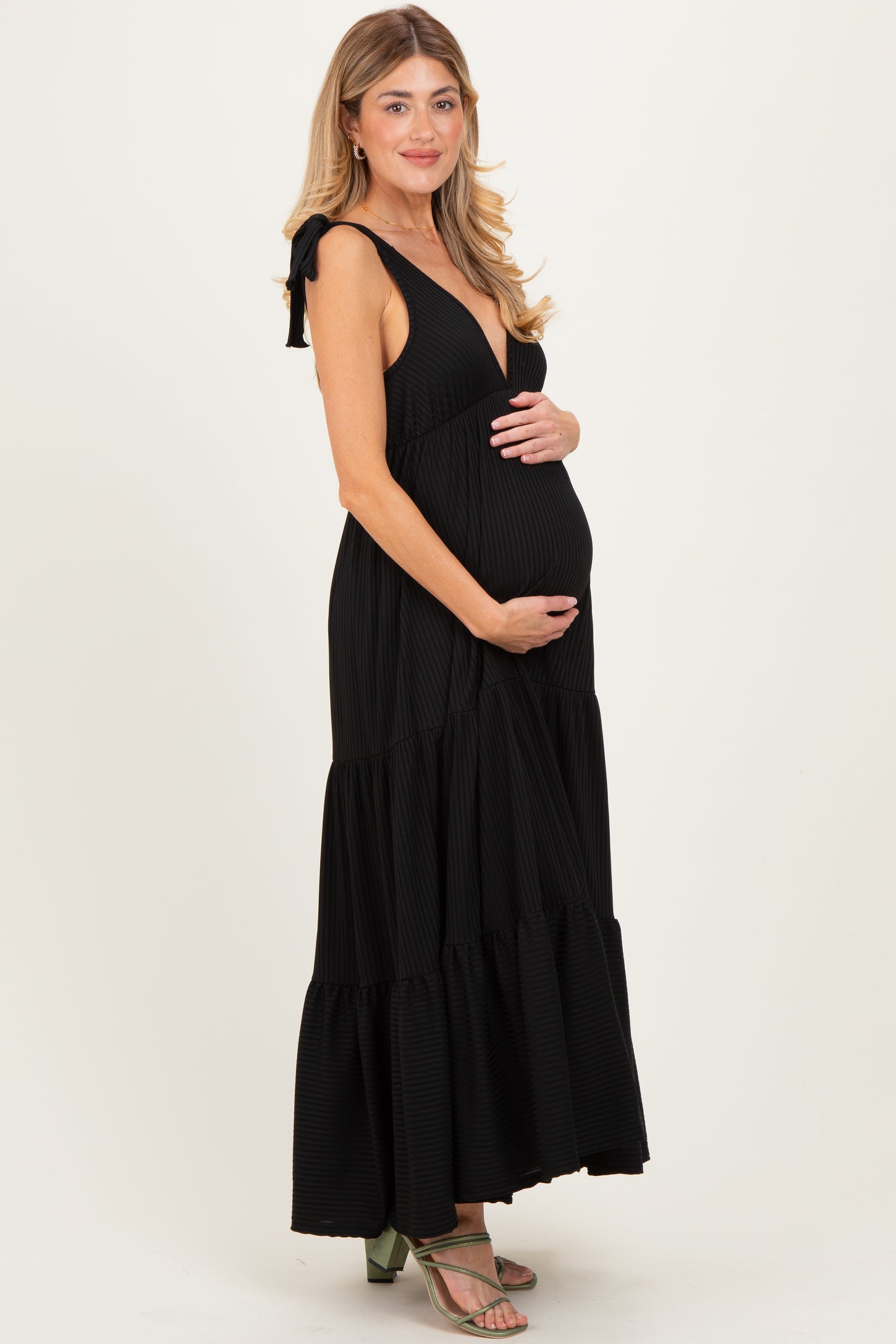 woman wearing a black striped maternity maxi dress with a deep v-neck and tied straps, holding her baby bump