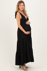 woman wearing a black striped maternity maxi dress with a deep v-neck and tied straps, holding her baby bump