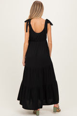 woman wearing a black tiered maxi maternity dress with tie shoulder straps and a flowing silhouette