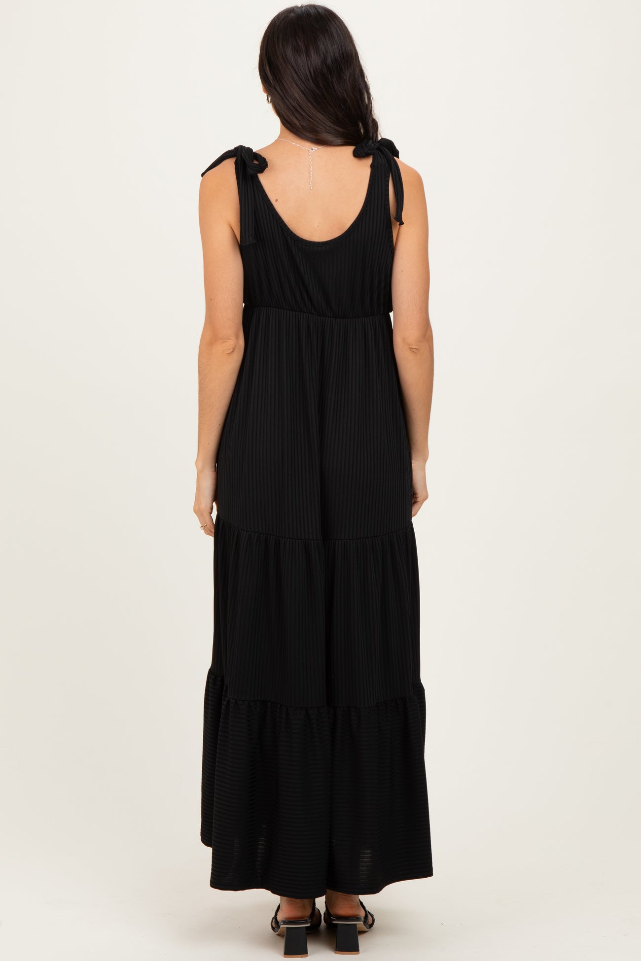 woman wearing a black tiered maxi dress with tie shoulder straps, shown from the back